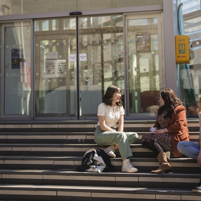 Three students sitting on the steps outside the Alex building