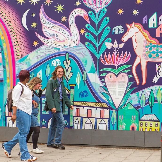 Three students walking in front of a wall mural