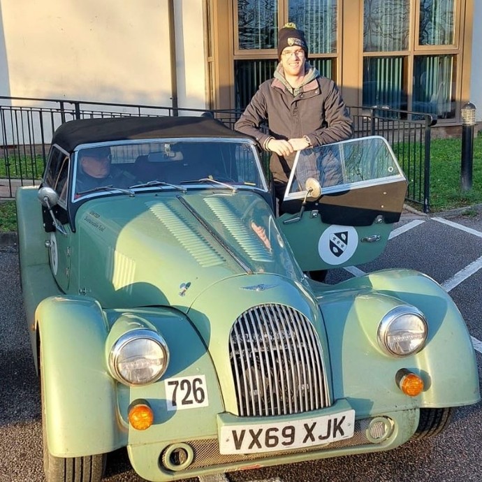 Tim Tudor stands leaning slightly on the door of a pale green Morgan Plus Four.