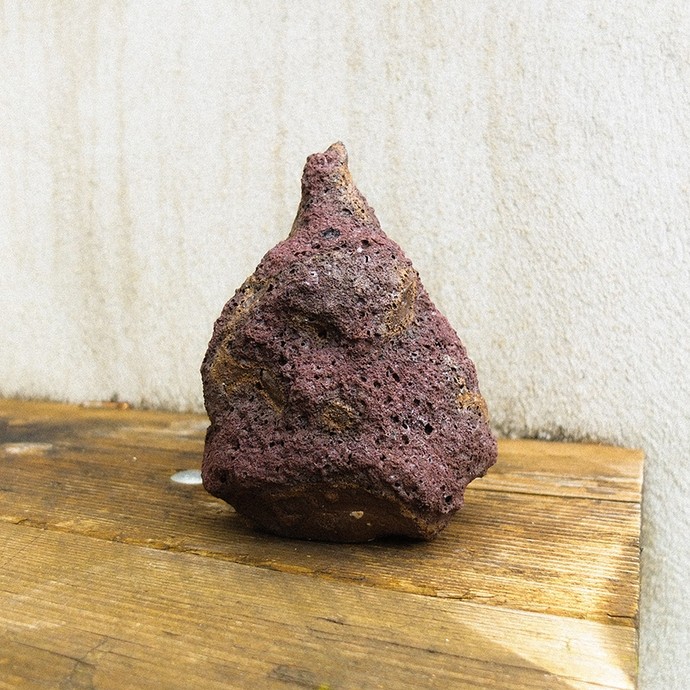 A conical reddish rock on a wooden bench outdoors.