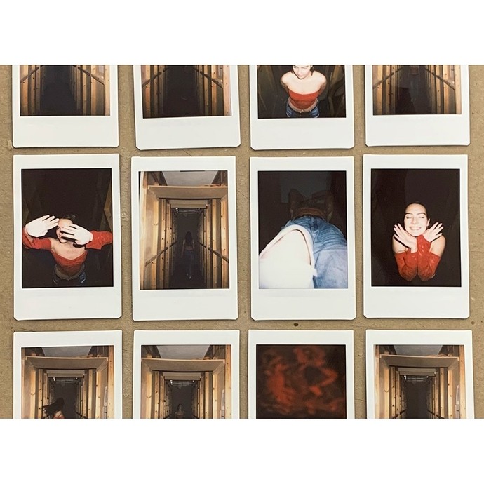 Twelve polaroid-style photos fixed to a piece of board in rows of four; most show a young woman in a red top walking through a wooden tunnel or striking poses in the dark.